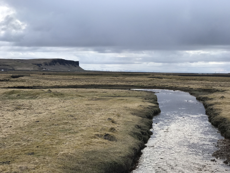 A vast expanse of flat land with a small creek in the middle and a cliff in the background.