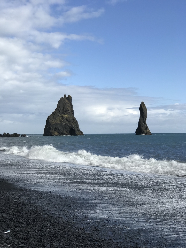 Large rock formations rising from the ocean with waves crashing at their base.