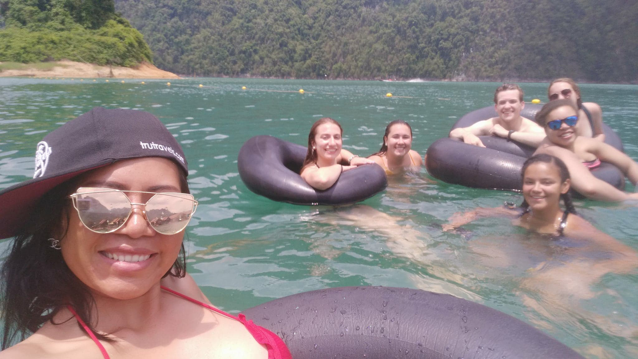 A group of people floating with inner tubes in water surrounded by greenery.