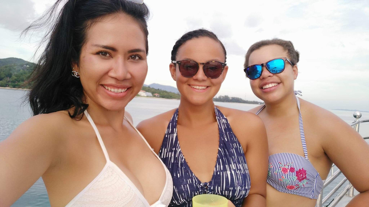 Three women smiling on a boat with ocean in the background.