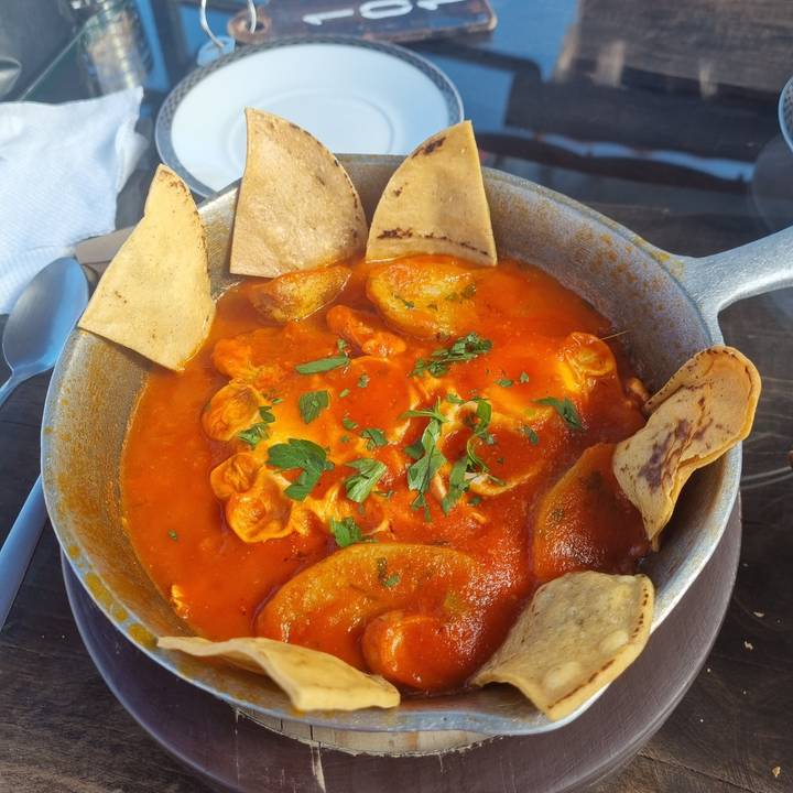 A bowl of food topped with herbs and accompanied by tortillas.