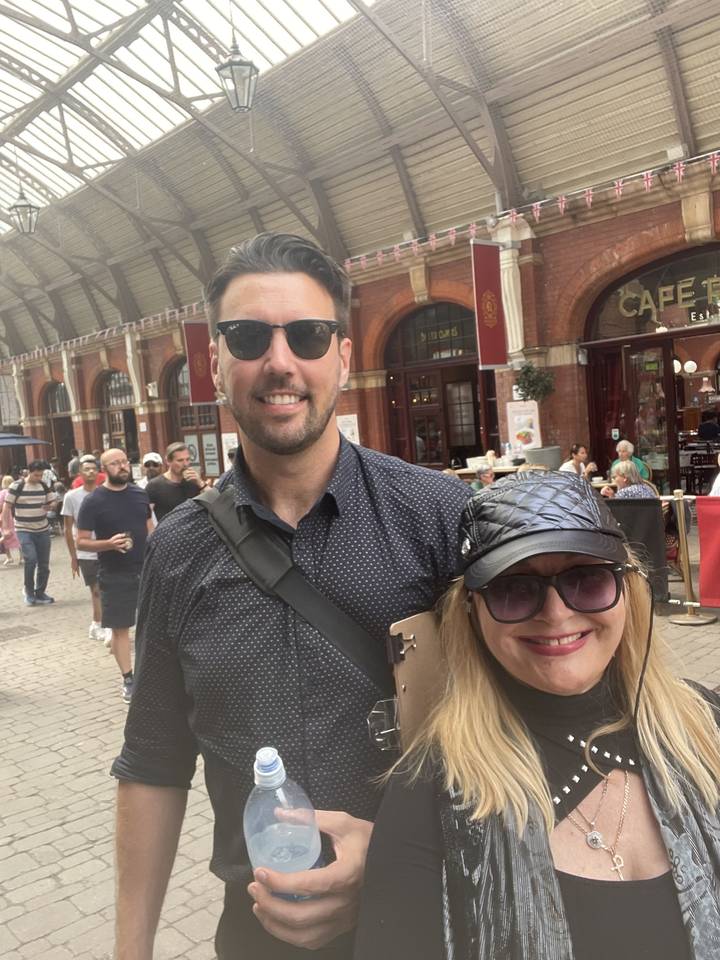 Two people smiling in front of a historical train station.