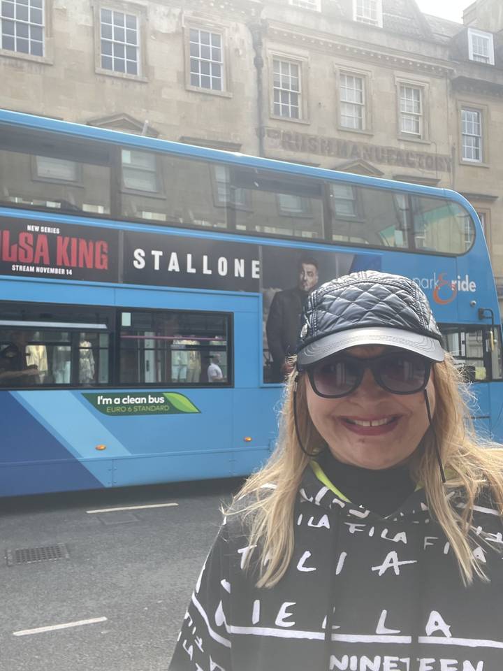 Woman posing next to a blue bus with urban background.