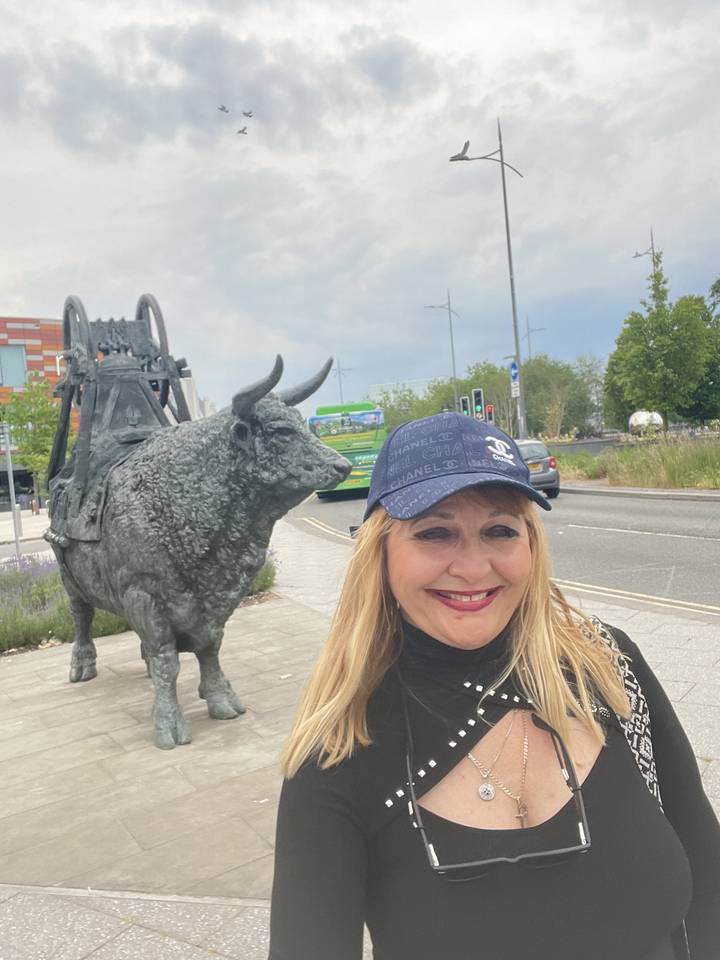 Woman posing next to a bull statue on a street.