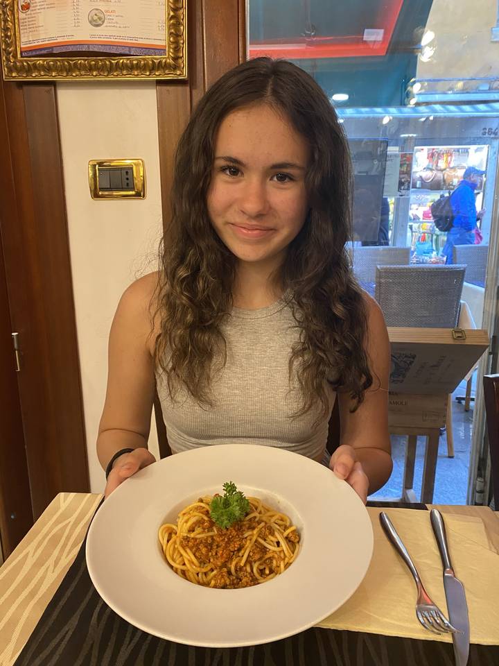 Person presenting a dish of pasta at a restaurant table.