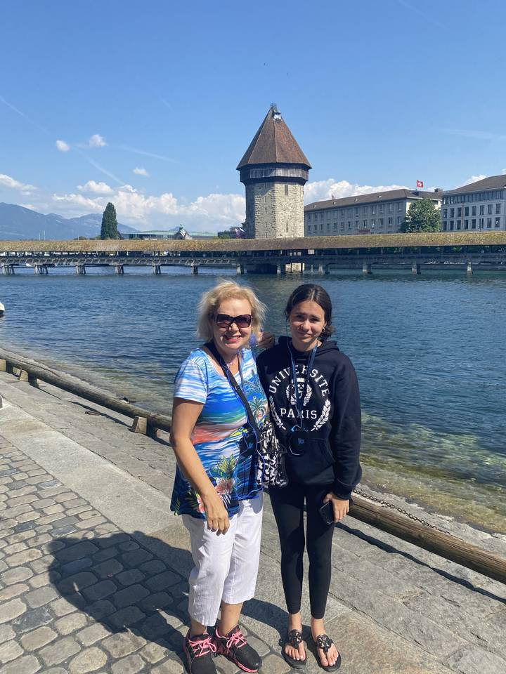Two people posing by a historic structure with a river.