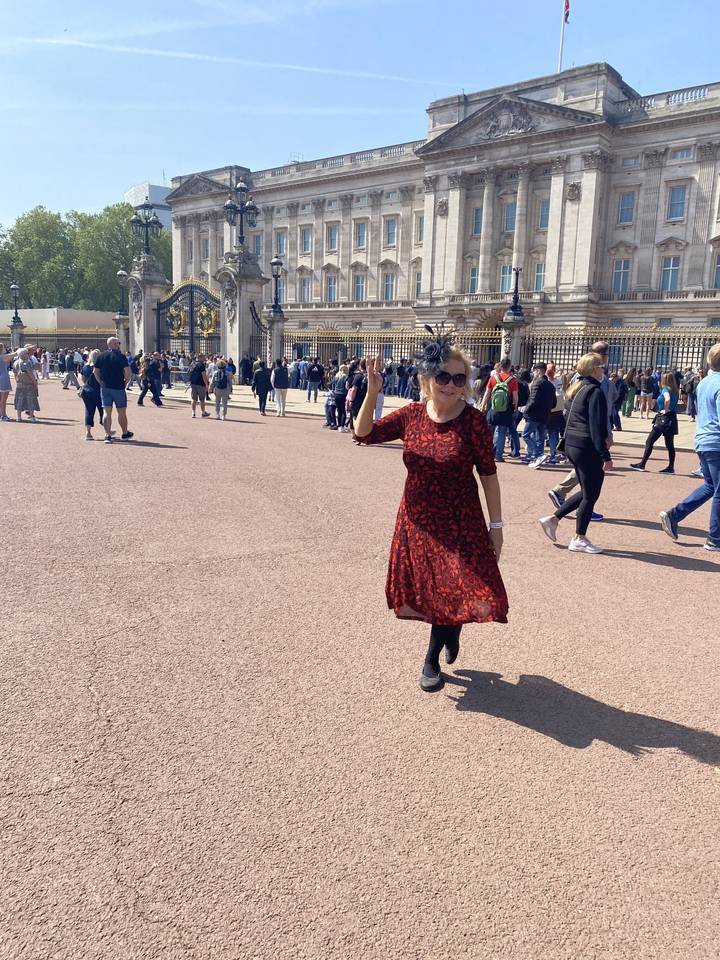 Person posing in front of Buckingham Palace with crowds around.