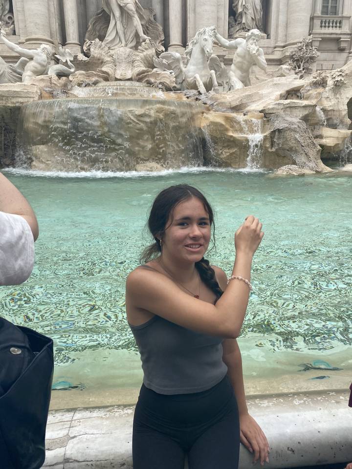 Person posing by Trevi Fountain with marble statues in the background.