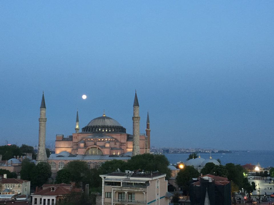 Illuminated historic mosque under a clear evening sky with the moon.