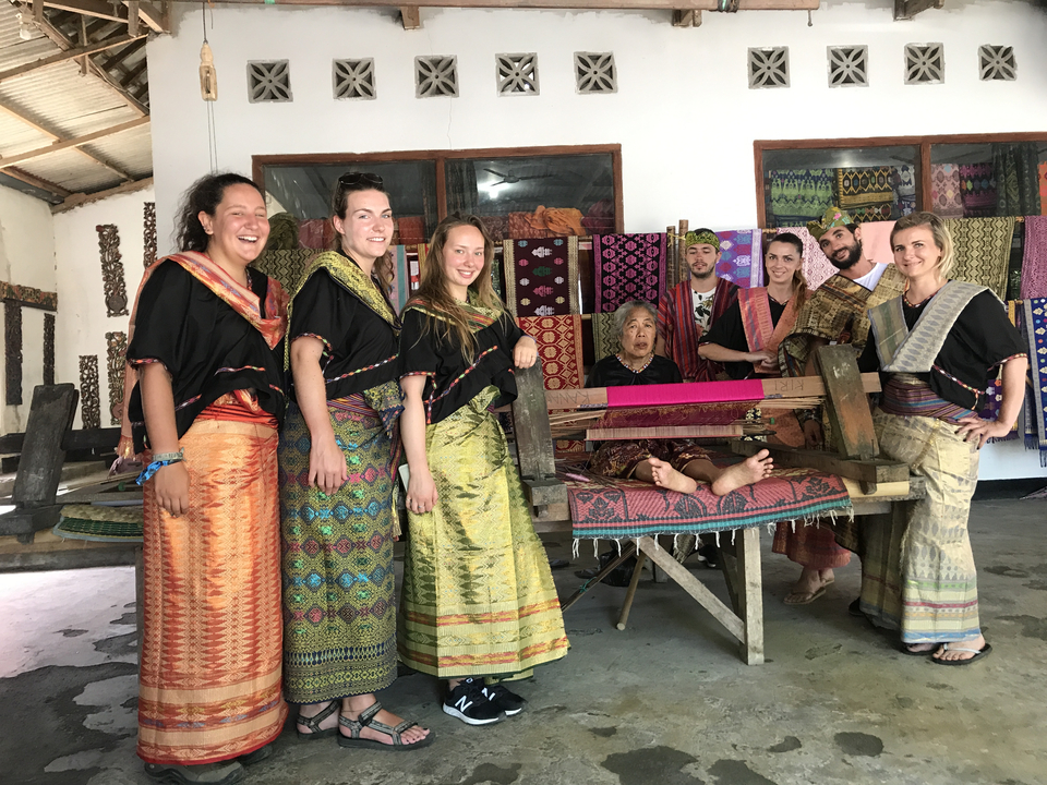 Group of people in traditional clothing inside a textile workshop.