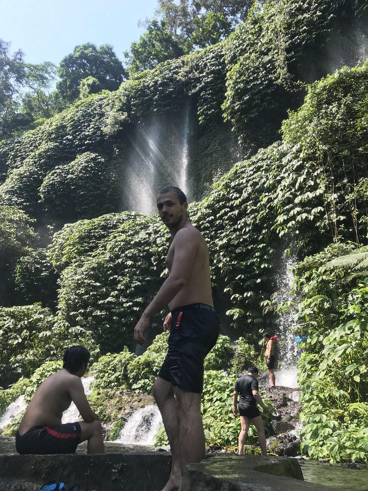 Man standing near a waterfall in a lush forest.