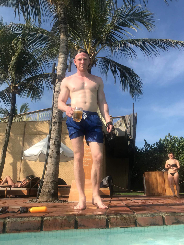 Man standing by the poolside with a drink.