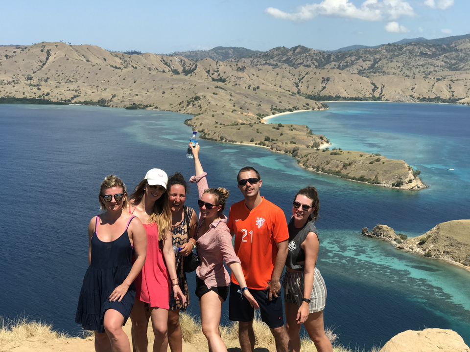 Group posing at a scenic viewpoint with ocean and mountains.