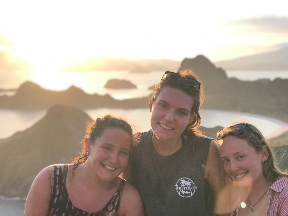 Three women posing during sunset with scenic hills in the background.
