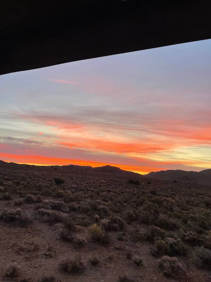 Vibrant sunset over a hilly and scrubland landscape.