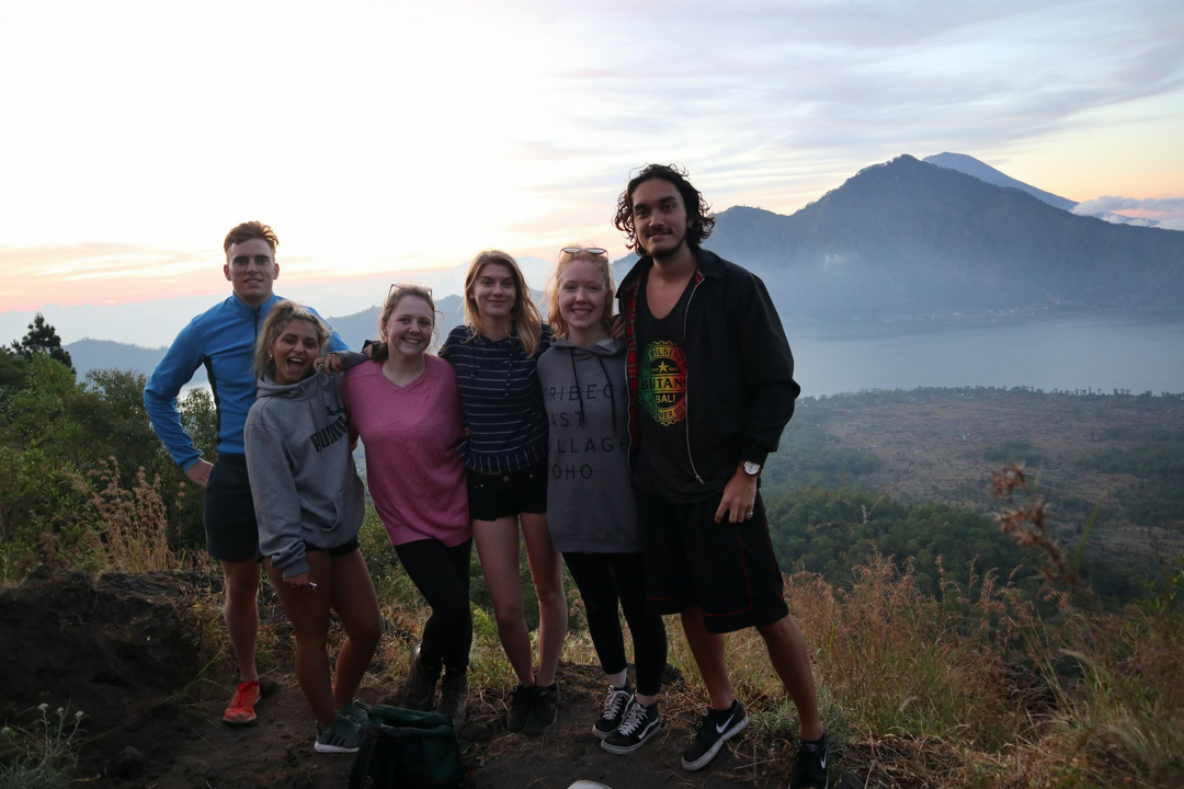 Group of people posing on a mountain summit with a view of a lake.
