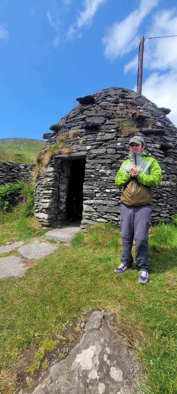 Person standing in front of a traditional stone beehive hut.