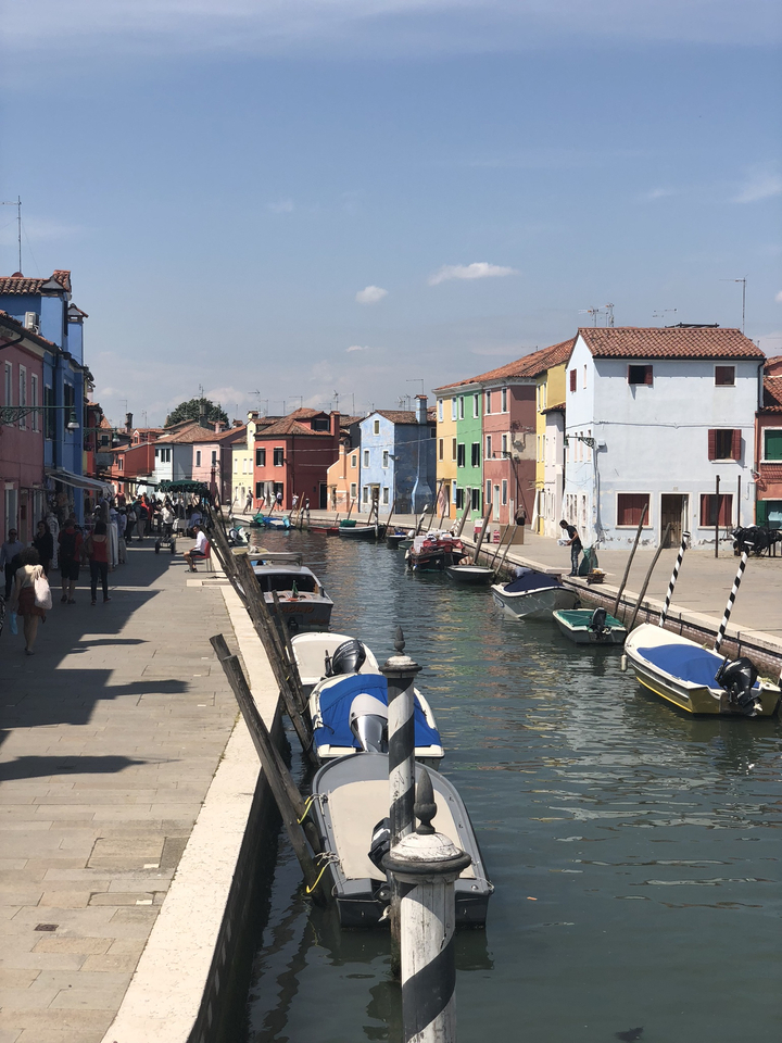 Colorful buildings along a canal with boats and people walking along the pathway.