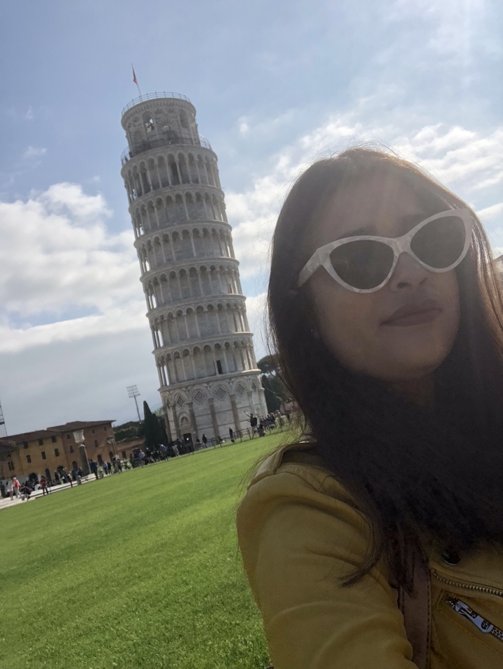Tourist taking a selfie with the Leaning Tower of Pisa in the background.