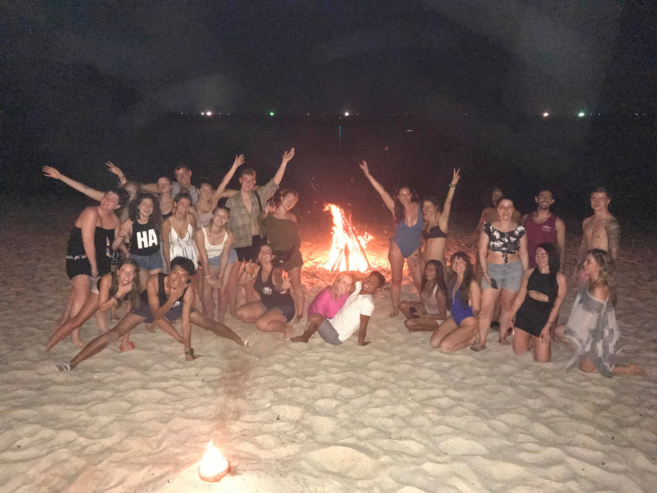 Group of people around a bonfire on the beach at night.