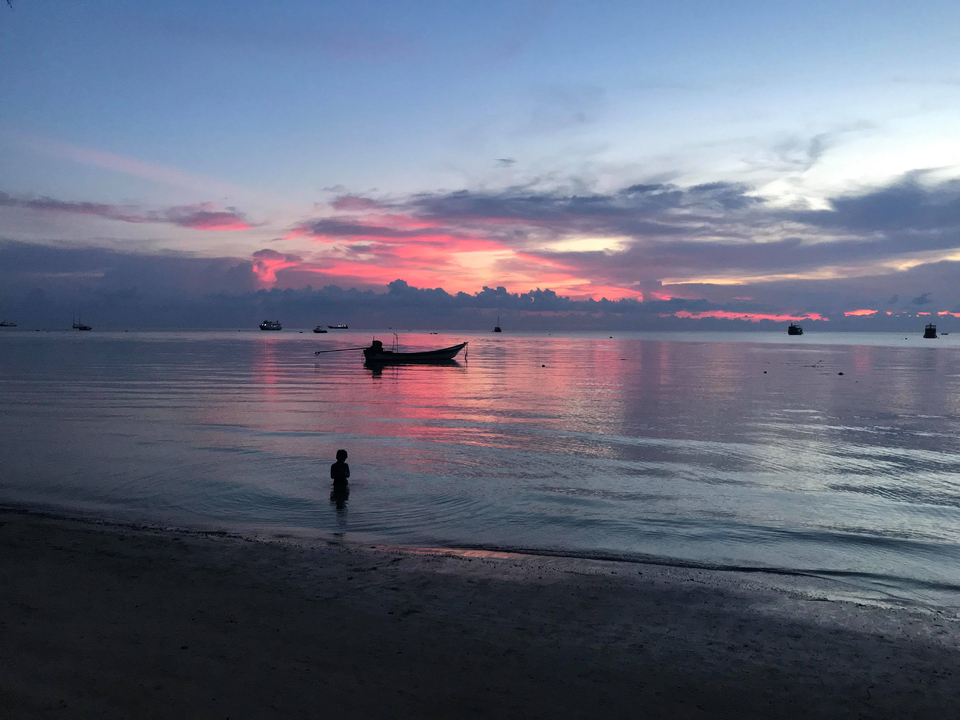 Silhouette of a child on the beach during a vibrant sunset with a boat.