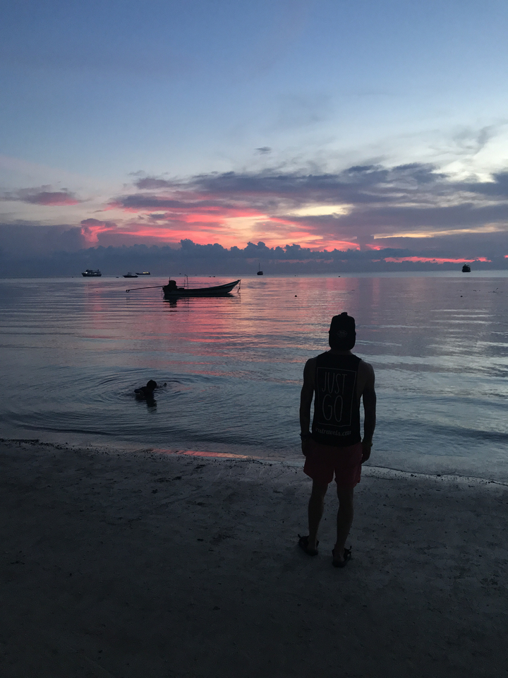Silhouette of a person at sunset with a boat and dramatic sky.