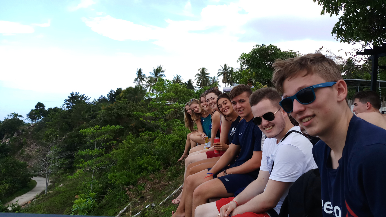 Group sitting on a ledge with a view of trees and sky.