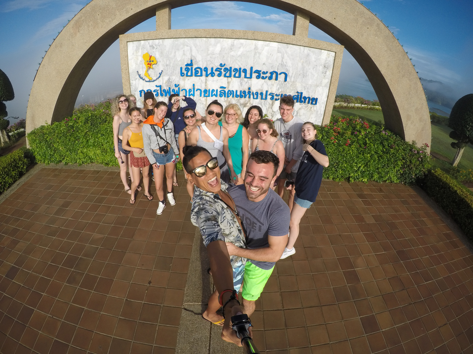 Group selfie at a scenic viewpoint with a sign in the background.