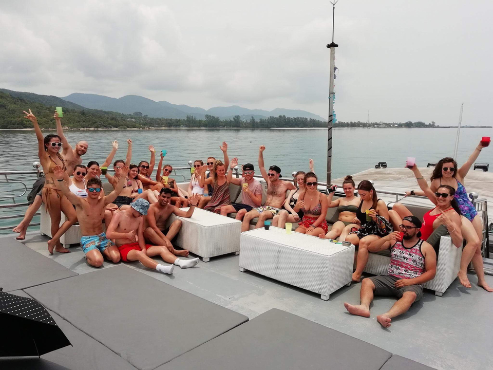 Large group posing on a boat with hills in the background.