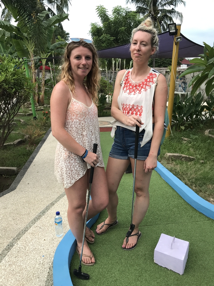 Two people standing on a mini-golf course with clubs.