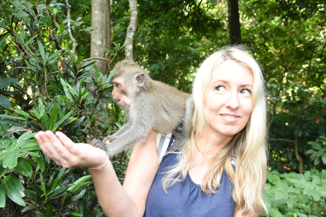 Blonde woman with a monkey on her shoulder in a forest.