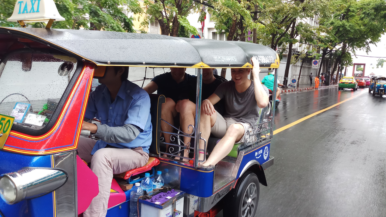 People riding in a tuk-tuk on a rainy street.