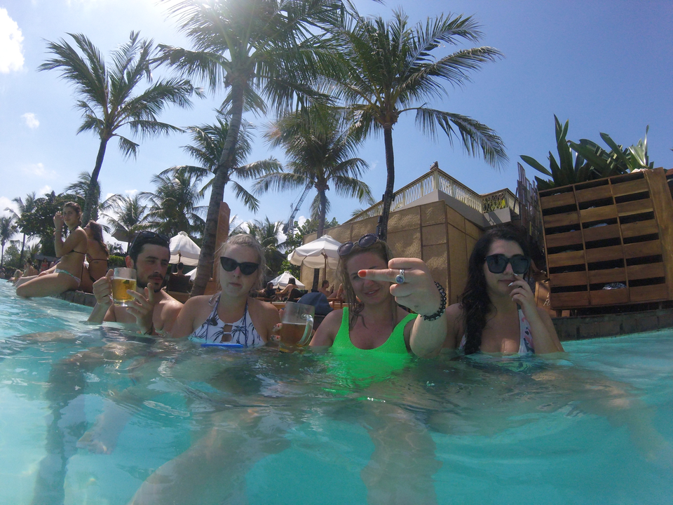 Group of people enjoying drinks in a swimming pool surrounded by palm trees.
