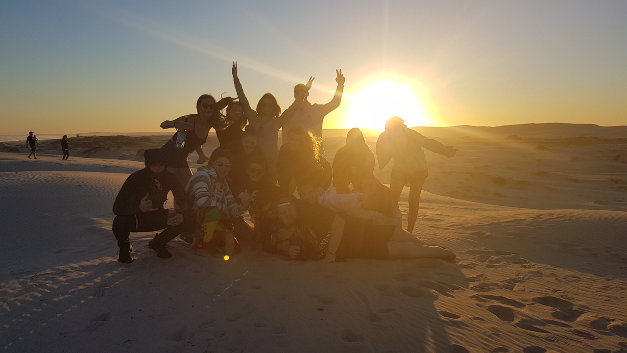 Group of people on sand dunes during sunset.