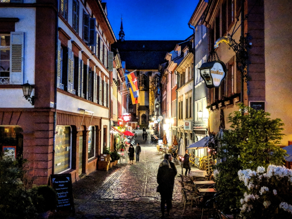 Une charmante rue pavée avec des drapeaux et des gens qui marchent, bordée de bâtiments colorés.