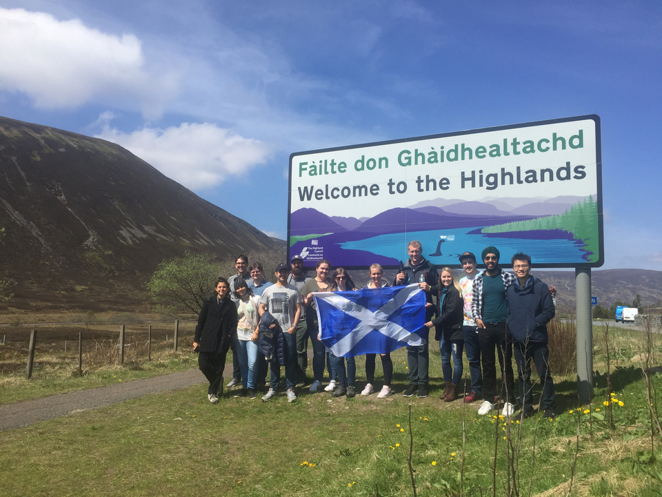 Group posing with Scottish flag in front of a welcome sign.