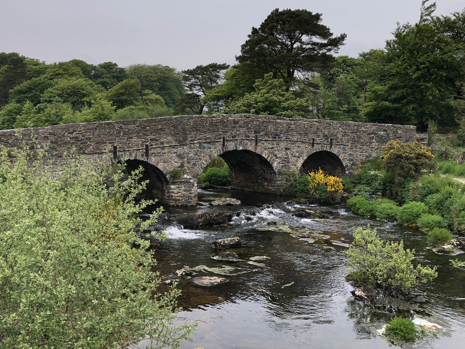 An old stone bridge crossing over a flowing river in a lush green landscape.