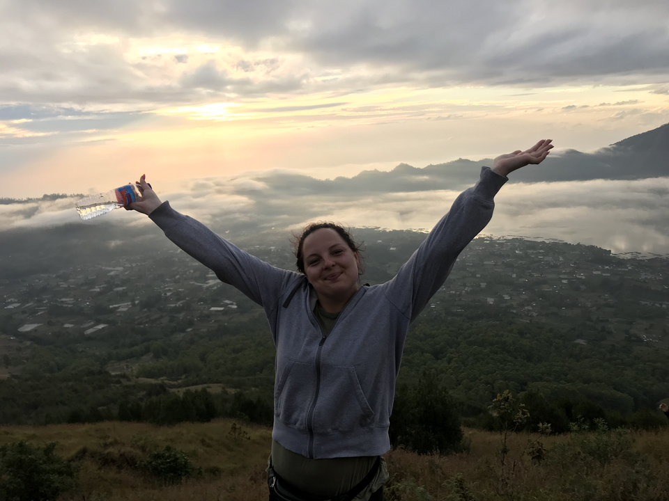 A woman standing on a mountain with her arms raised triumphantly over a foggy valley.