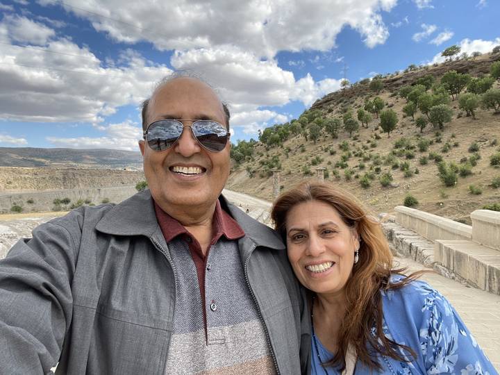 Couple posing in front of a hill with trees.