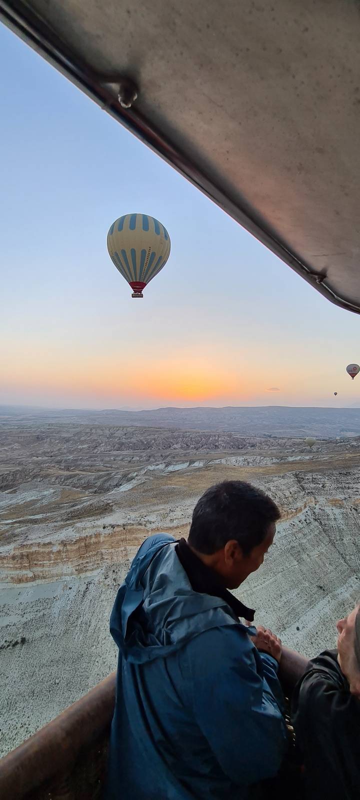 Hot air balloon and person in a basket during sunrise over a rocky landscape.