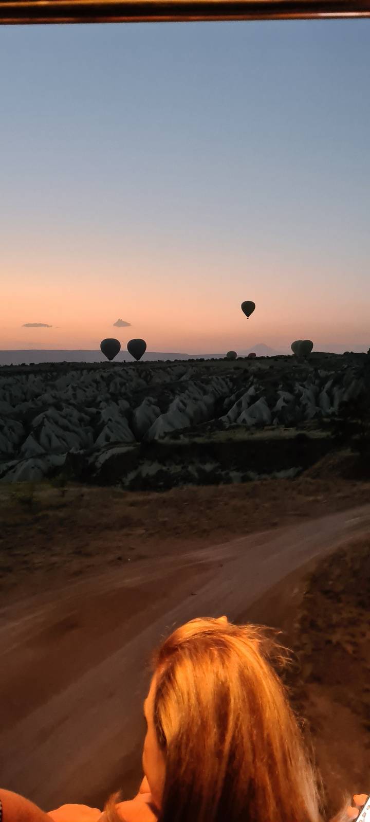 Sunset with hot air balloons and partial view of a person in a landscape with rock formations.