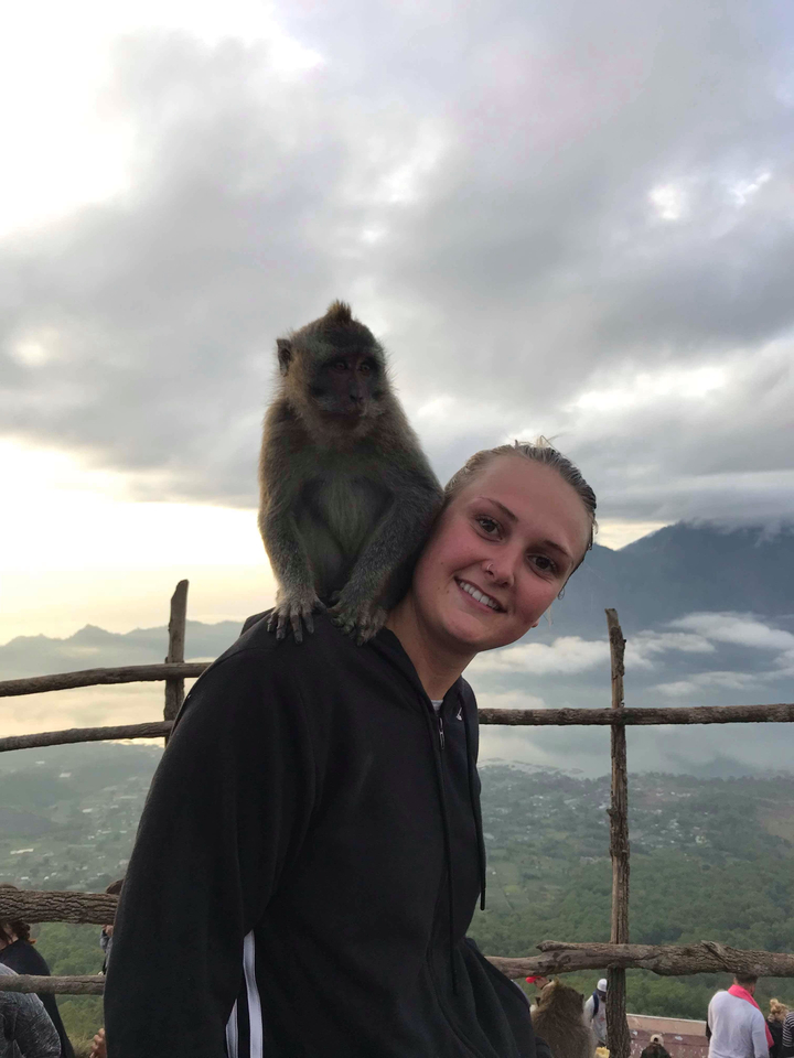 A person smiling with a monkey sitting on their shoulder with a misty mountain view.