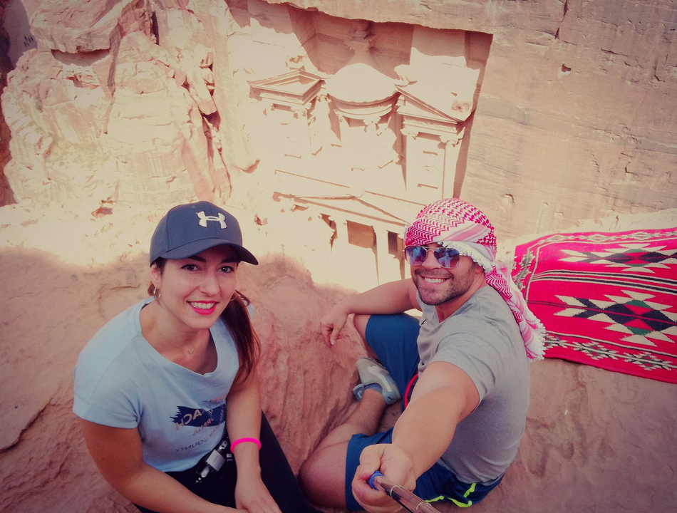 Couple sitting on a cliff overlooking the rock-carved treasury building.