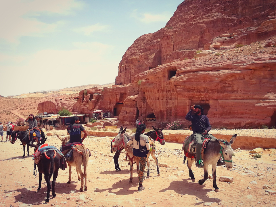 People riding donkeys in a Petra-like desert landscape.