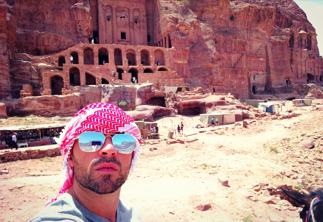 Person with sunglasses posing at the Petra Treasury with rock formations visible.