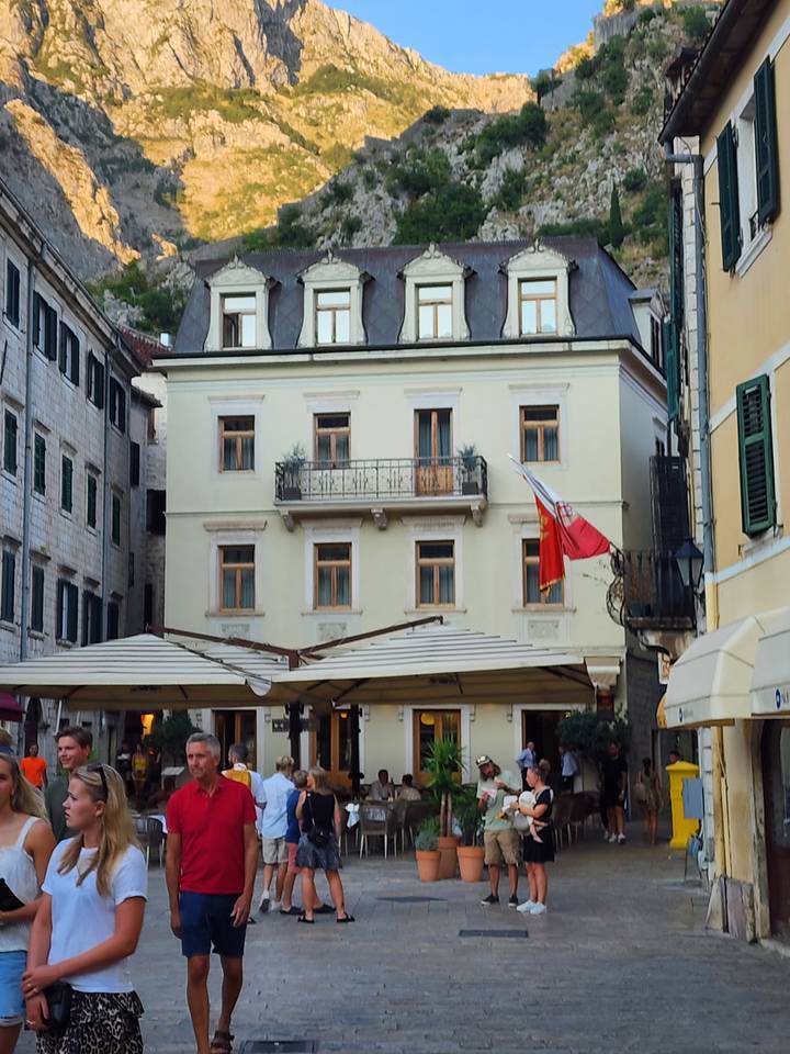 Street view with a building displaying a flag and outdoor cafe.