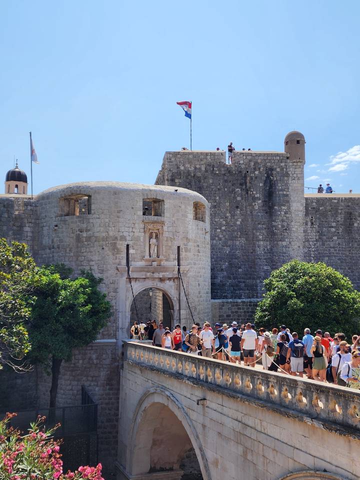 Historic stone fortress with tourists viewing from a bridge.
