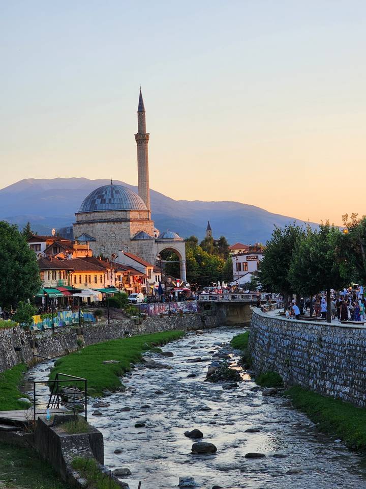 Historic mosque near a river with mountains in background.