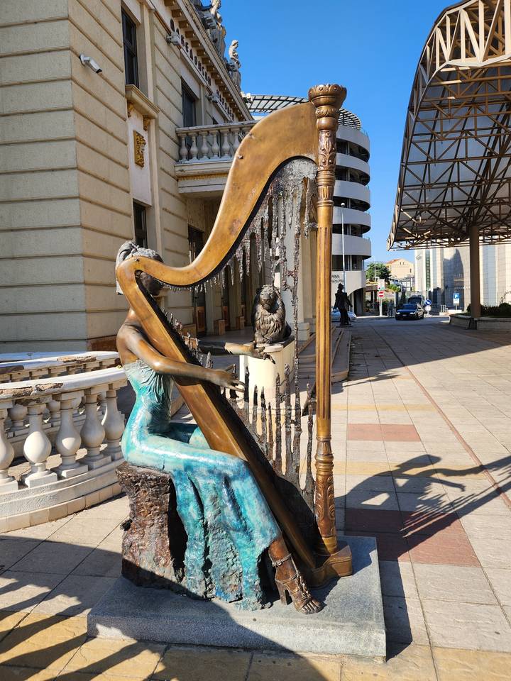 Statue of a musician playing a harp in an urban area.