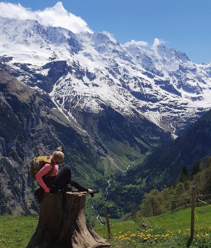 A hiker sitting on a ledge overlooking a snow-capped mountain range.